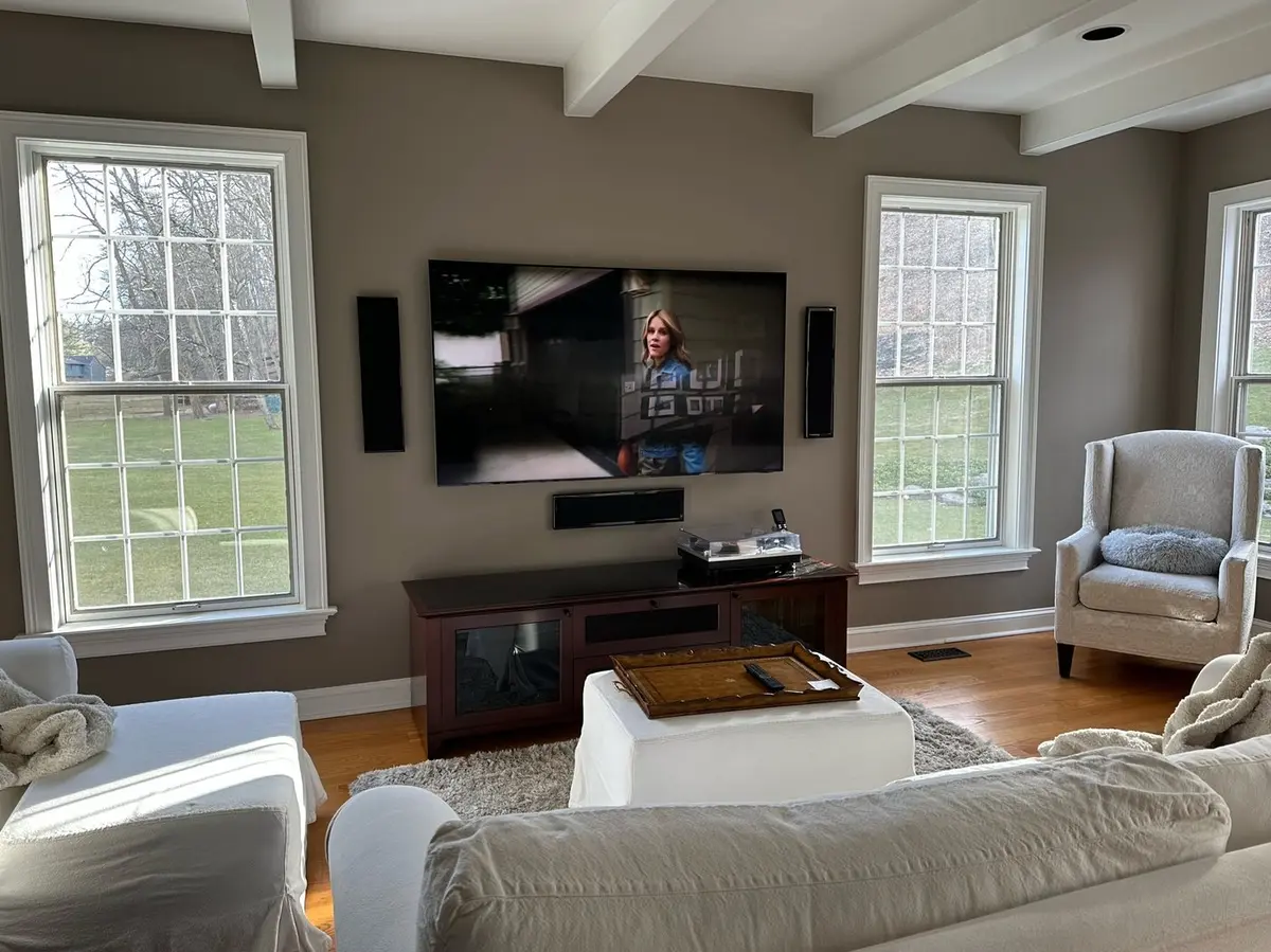 Mounted TV with flanking in-wall speakers and center soundbar in a bright living room